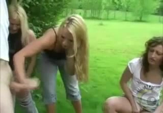 Three babes stimulate a man's penis with their hands in a field